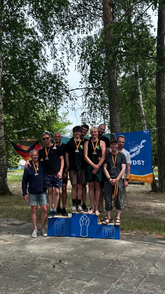 Podium bei der Siegerehrung der Disziplin "Manschaftstreffübung" der Deutschen Meisterschaft. Mannschaft 1 des TCDM, bestehend aus Maik, Nick, Eric und Matteo, stehen zusammengedrängt auf dem obersten Treppchen. Alle haben jeweils 1 Goldmedaille um den Hals.